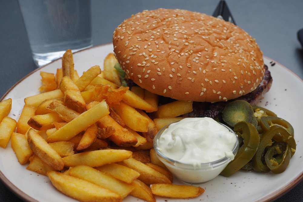 Burger wołowy z papryczkami jalapeño, frytki i miseczka sosu na talerzu