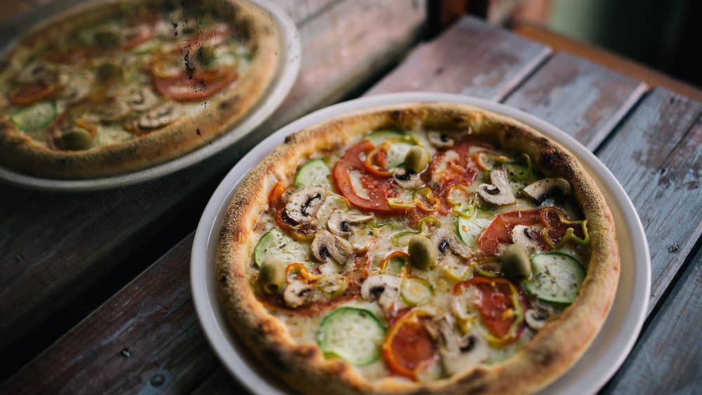 Pizza z pieczarkami, cukinią i oliwkami na postarzanym drewnianym stole w restauracji