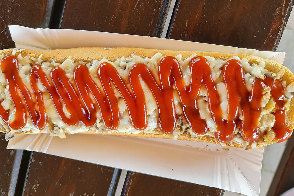 Zapiekanka na bagietce z pieczarkami, roztopionym serem i ketchupem, na papierowej tacce